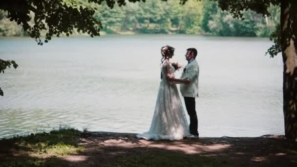 Vue latérale d'un couple embrassant le jour de leur mariage. Mariée et marié heureux dans un bel endroit sur une rive de la rivière . — Video