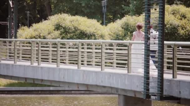 Gelukkige paar lopen op een brug op de trouwdag. Achteraanzicht van de mooie bruid en bruidegom, hand in hand. Steadicam schot — Stockvideo
