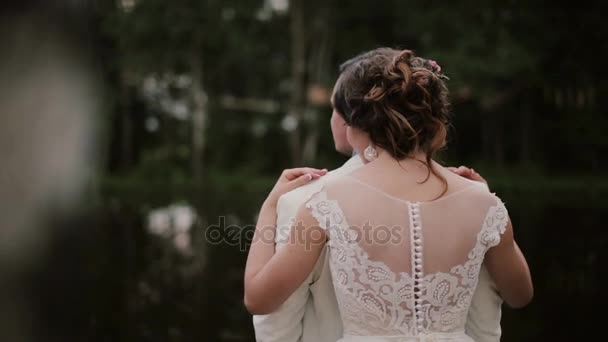 Lovers peacefully standing together. Bride hugs her groom standing behind him. Woman in a pretty white dress. Back view — Stock Video