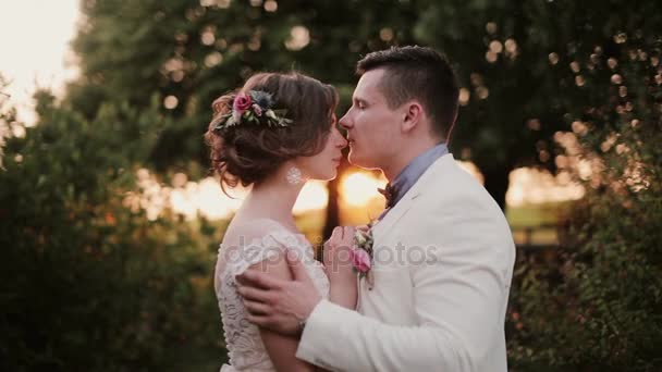 Os amantes felizes beijam ao pôr-do-sol no lugar muito pitoresco no dia do casamento. Bela vista dos amantes na natureza. Vista lateral — Vídeo de Stock