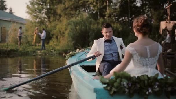 Los amantes se divierten el día de su boda. Pareja enamorada en un barco azul amarrando a una orilla del río. remos de novio . — Vídeos de Stock