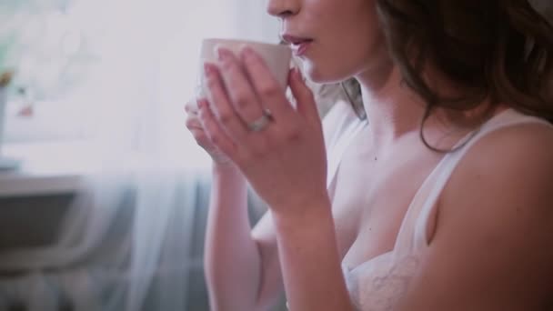 Närbild av kvinna i natt klänning sitter nära fönstret och dricka kaffe. Attraktiva flicka har frukost hemma. — Stockvideo