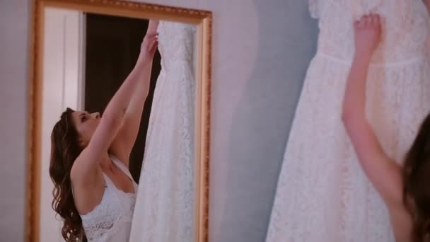 Reflectie in de spiegel. Jonge vrouw opstijgt in een trouwjurk van een hanger. Ochtend ceremonie voorbereiden. — Stockvideo
