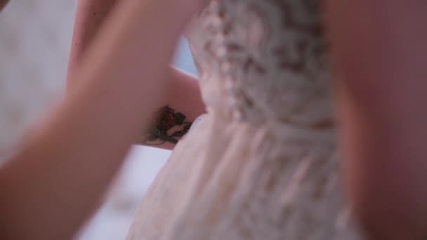 Dama de honor ayudando a ponerse el vestido de novia, botones de la parte posterior. Preparación matutina de novia joven con tatuaje . — Vídeo de stock
