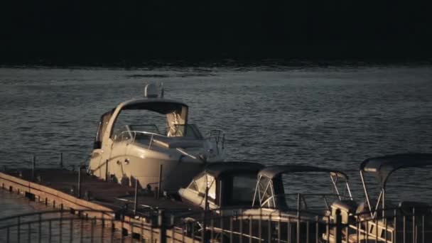 Ξύλινη προβλήτα στο ηλιοβασίλεμα το βράδυ. Μηχανοκίνητο σκάφος στέκεται κοντά στην ακτή. Ήρεμο χρόνο στη φύση, κύματα στον ποταμό. — Αρχείο Βίντεο