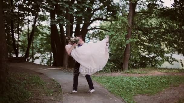 スタイリッシュな花嫁と花婿の公園で。新郎彼の腕の彼の花嫁を取るし、周りまんじ。幸せな恋人たちが結婚式の日を共有します。. — ストック動画