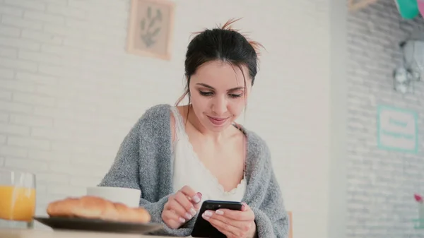 Закрытый вид женщины, завтракающей и просматривающей Интернет, используя сенсорный экран. Девушка читает новые на смартфоне и улыбается . — стоковое фото