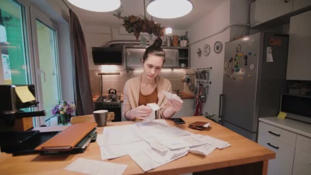 Mujer joven sentada a la mesa en la cocina y calculando facturas después de comprar. Departamento de cuentas locales . — Vídeo de stock