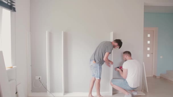 Two young man do the repairs in the bright apartment. Men assemble furniture together. — Stock Video
