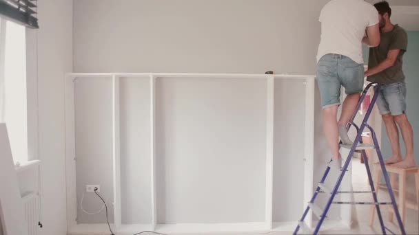 Dos hombres reparando en la habitación luminosa. Hombre ayudando a su amigo a mudarse a una casa nueva, ensamblar muebles juntos . — Vídeos de Stock