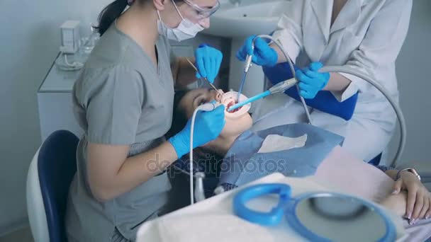 Jonge vrouw zittend in tandheelkundige stoel. Arts met tandheelkundig verpleegkundige behandeling van een patiënt, schalen en polijsten van de tanden. — Stockvideo