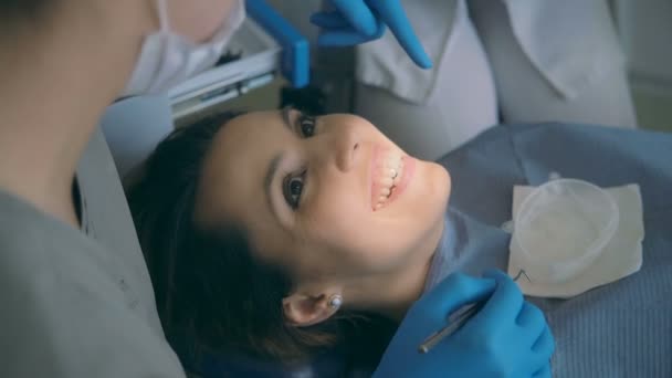 Junge Frau sitzt im Zahnarztstuhl und spricht mit dem Arzt. Frau lächelt und lacht beim Zahnarzt. — Stockvideo