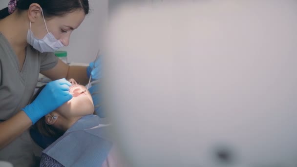Плановое обследование у врача. Молодая женщина лежит в стоматологическом кресле, пока дантист проверяет ее зубы . — стоковое видео