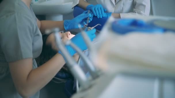 Молодая женщина лежит в стоматологическом кресле. Стоматолог очищает полость рта, используя зеркало и двигатель сверления . — стоковое видео