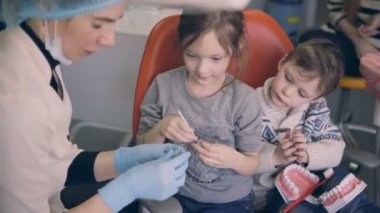 Diş check-up önce dişçi sandalyede oturan iki çocuk. Genç doktor ile kardeş kalıp.