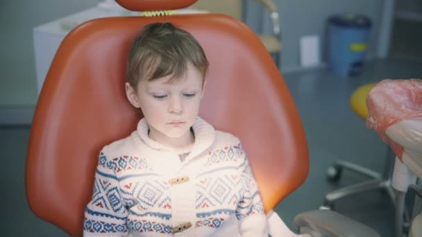 Милый маленький мальчик в кабинете доктора и ждет. Мужчина смотрит вокруг сидя в кресле стоматолога перед стоматологическим осмотром . — стоковое видео