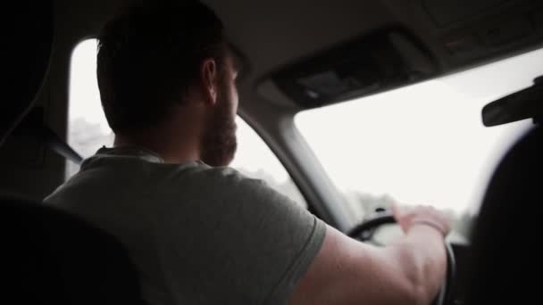 Una vista trasera de un hombre conduciendo un coche bajo la lluvia. Manos en el volante, limpiaparabrisas funcionando . — Vídeo de stock