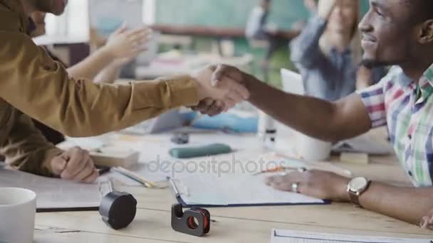 2 つのパートナー、アフリカ系と白人ビジネスマンは、手を振る。現代のオフィスで背景に拍手する人々 のグループ. — ストック動画