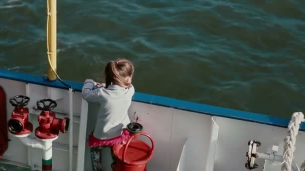 Маленька дівчинка стоїть близько до дошки корабельної палуби і дивиться на воду — стокове відео