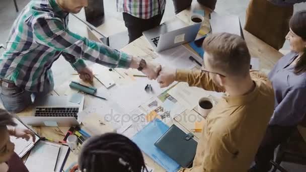 Bovenaanzicht van jonge business team samen te werken in de buurt van de tabel, brainstormen. Twee mans vuist begroeten elkaar. — Stockvideo