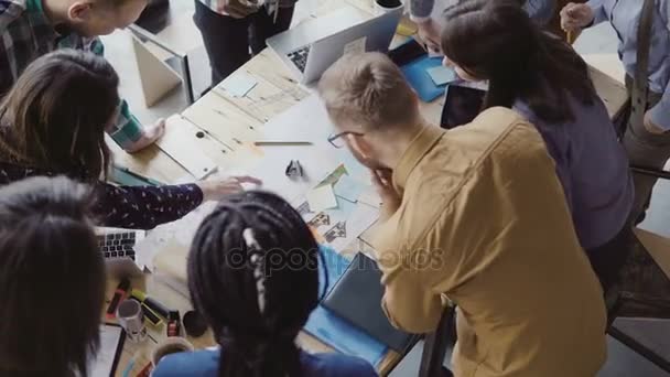 Blick von oben auf das junge Team, das an einem neuen Projekt arbeitet. Gruppe von Menschen gemischter Rassen, die am Tisch stehen und diskutieren. — Stockvideo