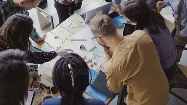 Visão superior da equipe jovem trabalhando em um novo projeto. Grupo de pessoas de raça mista em pé perto da mesa e discutir . — Vídeo de Stock