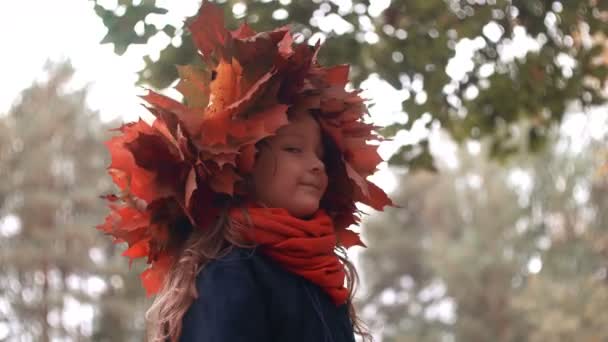 4k крупным планом портрет счастливой улыбающейся красивой маленькой девочки в венке из осенних кленовых листьев — стоковое видео