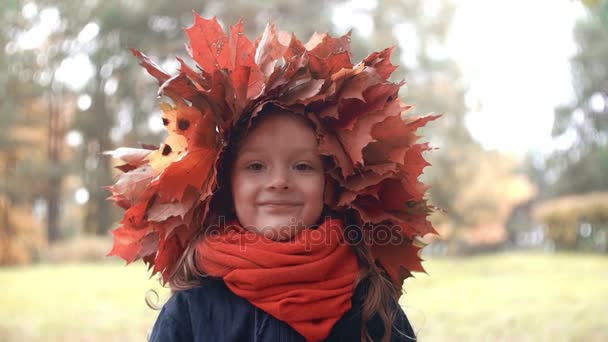 4 k närbild porträtt av leende söt liten flicka i en krans krona av höstlöv lönn poserar, gör roliga grimaser — Stockvideo