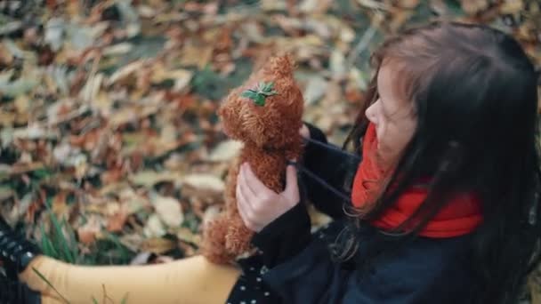 Niedliches kleines Mädchen, das mit ihrem Teddybär spielt, umarmt sie und hält sie auf dem Rasen im Herbstpark 4k — Stockvideo