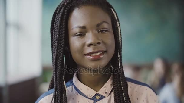 Retrato de una joven africana mirando a la cámara y sonriendo a una oficina moderna y ocupada. Empleado exitoso en el trabajo . — Vídeos de Stock