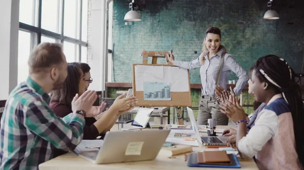 Reunión del equipo de negocios de carreras mixtas en la oficina del loft. Mujer gerente presentando datos financieros, grupo de personas aplaudiendo . — Foto de Stock