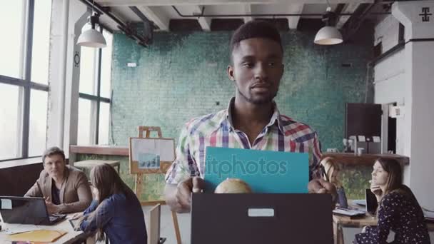 Jonge Afrikaanse man ontslagen van werk bij het opstarten. Man loopt via het Bureau, uitvoering doos met persoonlijke bezittingen. — Stockvideo