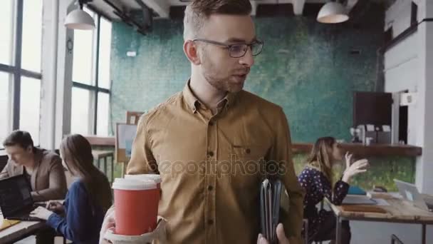 Beau directeur d'entreprise vient au bureau moderne au travail. Jeune homme accueille ses collègues, apporte du café à un ami .