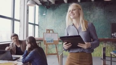 Modern ofis ve denetimleri bir çalışmayla çalışanın yürüyen genç sarışın takım lideri. Erkek kumaş örnekleri görünüyor.