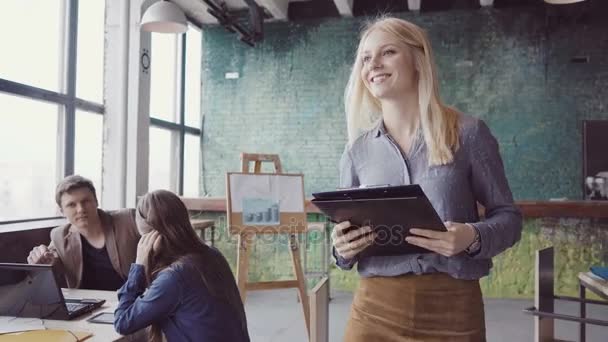 Jeune chef d'équipe blonde marchant à travers le bureau moderne et contrôle le travail de l'employé. Femme regarde les exemples de tissu .