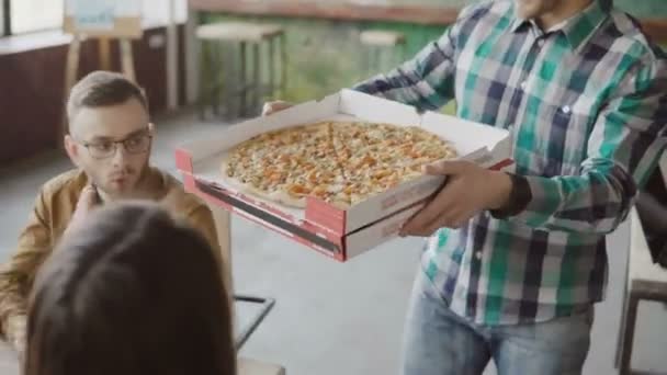 Giovane uomo d'affari porta la pizza al team di razza mista presso l'ufficio moderno. Felice gruppo di persone applaudono e sorridono . — Video Stock