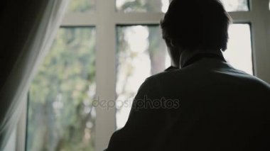 Pencere önünde duran ve bir iş için hazırlanıyor genç adam. Papyon beyaz gömlek ile erkek koyar.