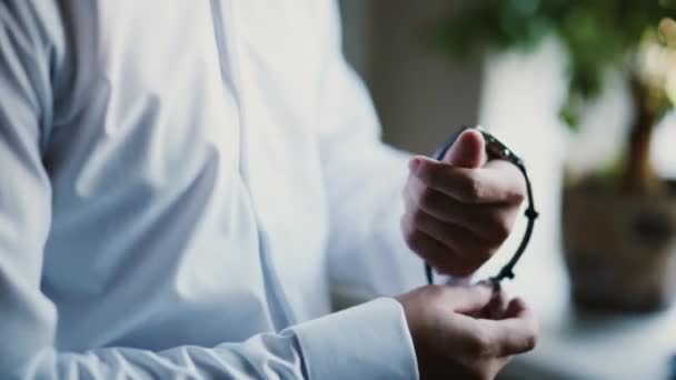 Man in a white shirt puts on a watch. Young businessman getting ready at the morning. Close-up view of male hands. — Stock Video