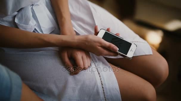 Zbliżenie młoda kobieta siedzi w szlafrok i za pomocą smartfonu. Kobieta dotyka ekranu, wygląda zdjęcie. — Wideo stockowe