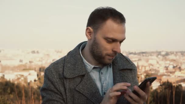 Porträt eines jungen, gut aussehenden Mannes am panorama von rom, italien. Männer nutzen das Smartphone draußen. — Stockvideo