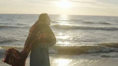 Sahilde günbatımı üzerinde yürüyen genç mutlu kadın. Ekose gergin Arms ile denizin kıyısında güzel kadın gider.