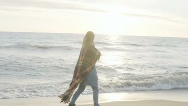 Mladá žena na břehu moře. Zamyšlená žena s plaid tráví čas sám na pláži v fouká chladný den. — Stock video