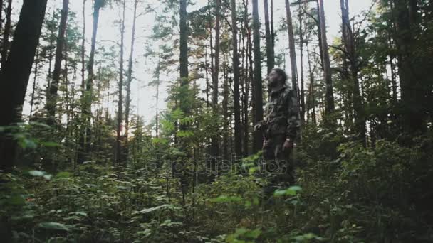 Νεαρός άνδρας στο καμουφλάζ στέκεται στο δάσος και κοιτάζοντας γύρω. Κυνηγός αρσενικό διερευνά το έδαφος για τη φύση. — Αρχείο Βίντεο