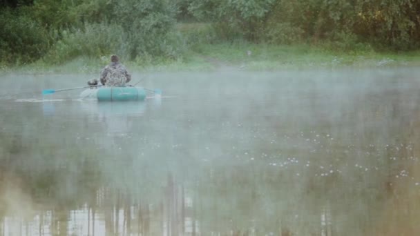 两个年轻人坐在橡皮船，早上用桨划船。湖上与雾在它的两名男. — 图库视频影像