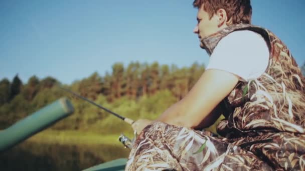 Seul jeune homme assis dans le bateau en caoutchouc et pêchant au lac. Homme tient la canne à pêche et tourne bobine de filature . — Video
