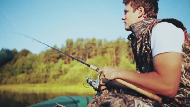 Solo joven sentado en el bote de goma y pescando en el lago. Macho sostiene la caña de pescar, captura el pez que muerde . — Vídeos de Stock