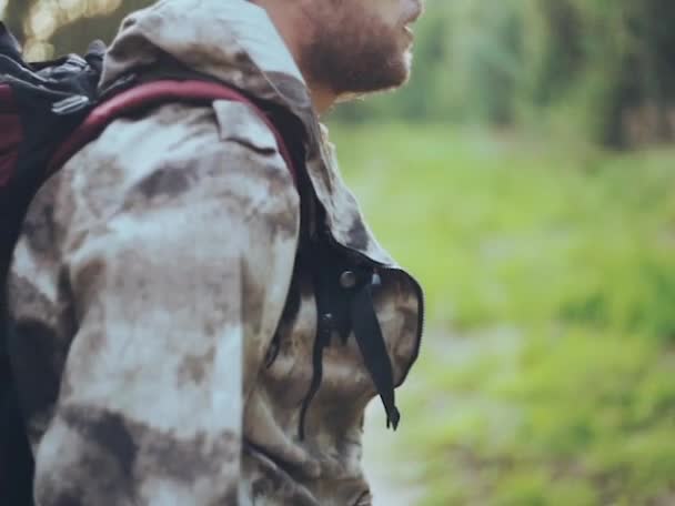 Närbild av ung man med ryggsäck titta runt i skogen. Hane i kamouflage unionalls utforska territorium. — Stockvideo