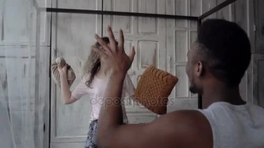 Erkek ve kadın sabah iyi eğlenceler. Çok ırklı çift pijama mücadele yastık tarafından var. Kaygısız zaman. Ağır çekim.