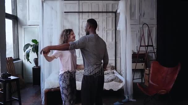 Multiraciale paar in pyjama dansen, plezier samen in de ochtend. Vrouw springt op man handen, kussen. Slow motion. — Stockvideo