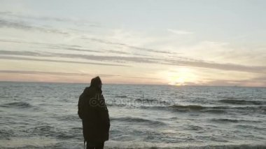 Deniz kıyısında ayakta ve günbatımı üzerinde seyir çekici genç adam. Plaj manzaraya sahip erkek.